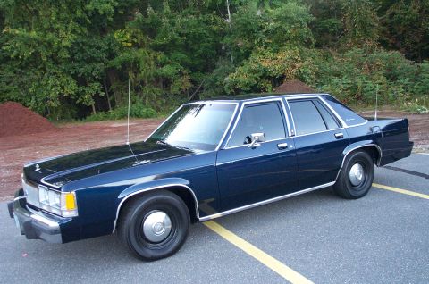 1991 Ford LTD Crown Victoria - This dark blue sedan, likely a 1990 model, is seen from a three-quarter front angle with dual antennas and chrome trim.
