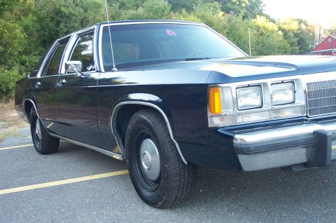 1991 Ford LTD Crown Victoria - Close low front three-quarter view of a dark blue boxy Ford full-size four-door sedan on black steel wheels with plain center caps, showing…