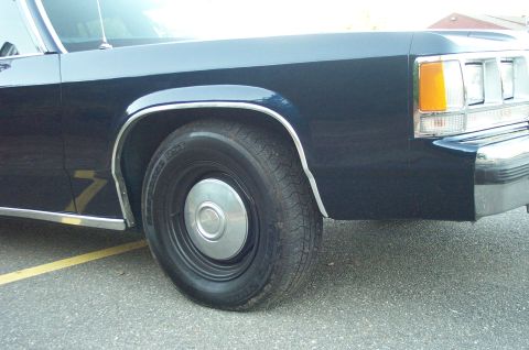 1991 Ford LTD Crown Victoria - Close-up of the front passenger side of a dark blue sedan, showing the wheel and headlight assembly.