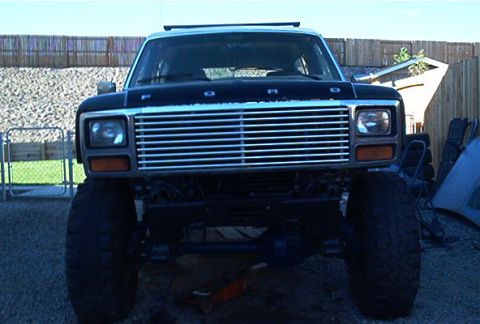 1986 Ford Bronco - This lifted Ford Bronco is parked outdoors with a fence and building in the background.