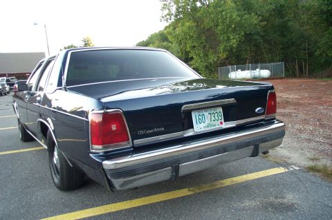 1991 Ford LTD Crown Victoria - A dark blue Ford LTD Crown Victoria sedan viewed from the rear three-quarter angle, parked in a lot with a New Hampshire 'Live Free or Die'…