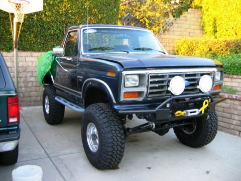 1985 Ford Bronco - A lifted Ford F-Series truck is parked in a driveway next to another vehicle.