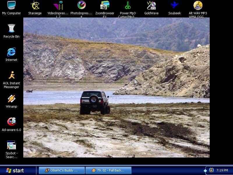 Dark two-door SUV with rear spare tire parked on muddy terrain near hills