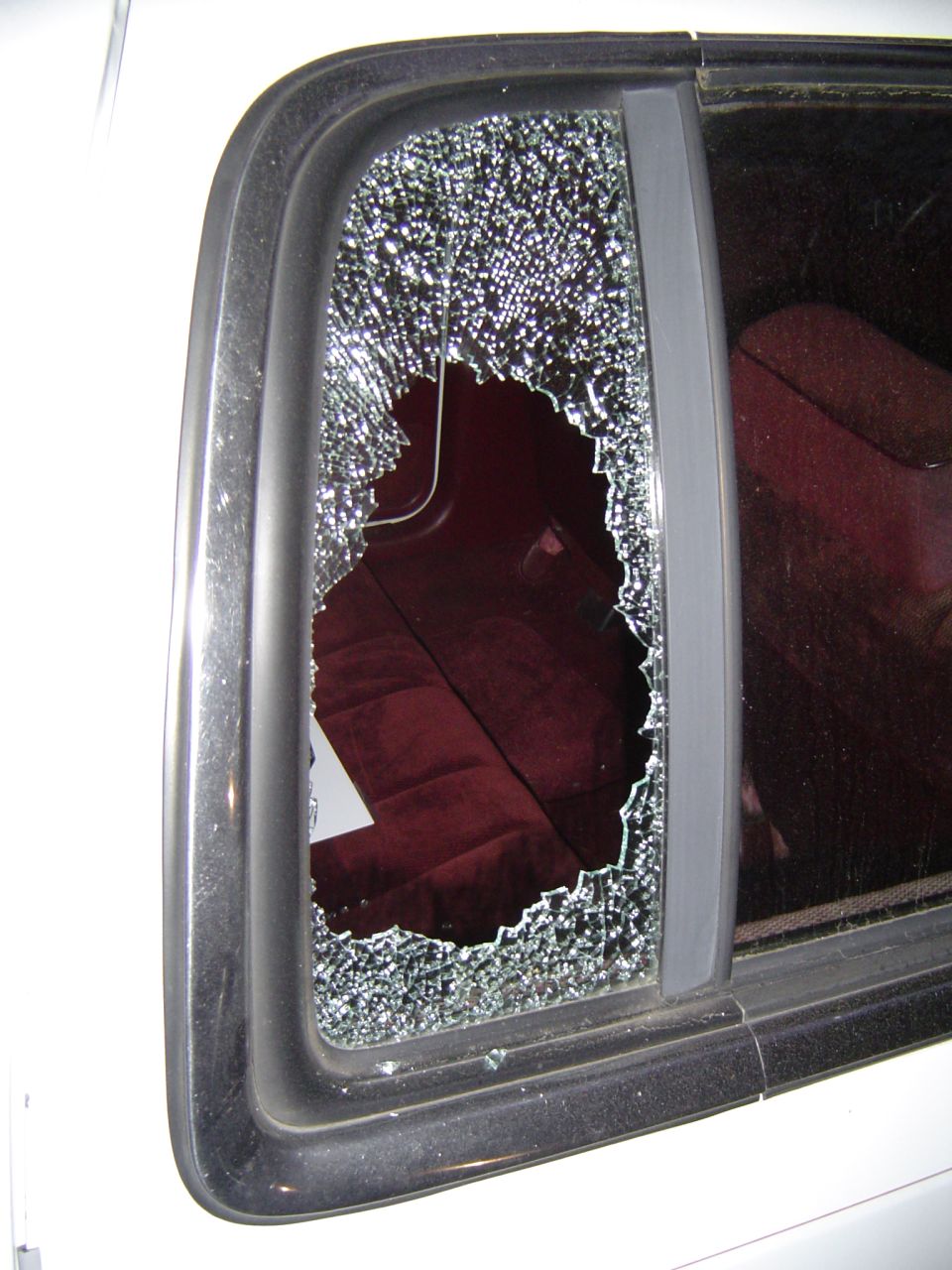 Smashed truck rear sliding-window glass shattered into a hole, red cloth seats visible inside