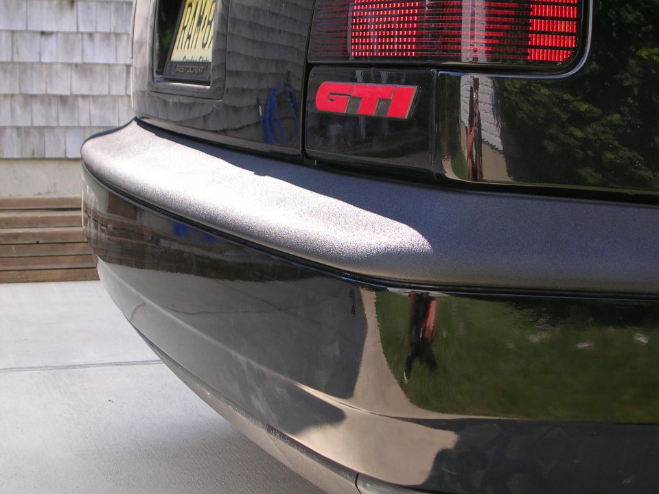 Dark VW GTI rear corner with red GTI badge and unpainted primer bumper section