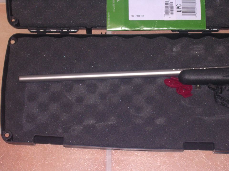 Rifle barrel and black grip in a foam-lined case with a green box on top