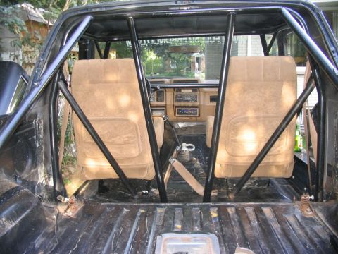 1986 Ford Bronco - The interior of an older SUV, modified with a roll cage, is viewed from the back.