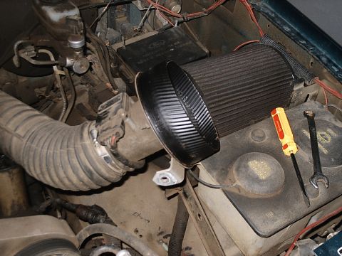 1996 Ford Bronco - Tools rest on the battery and coolant reservoir in a vehicle's engine bay, near an aftermarket air intake system.