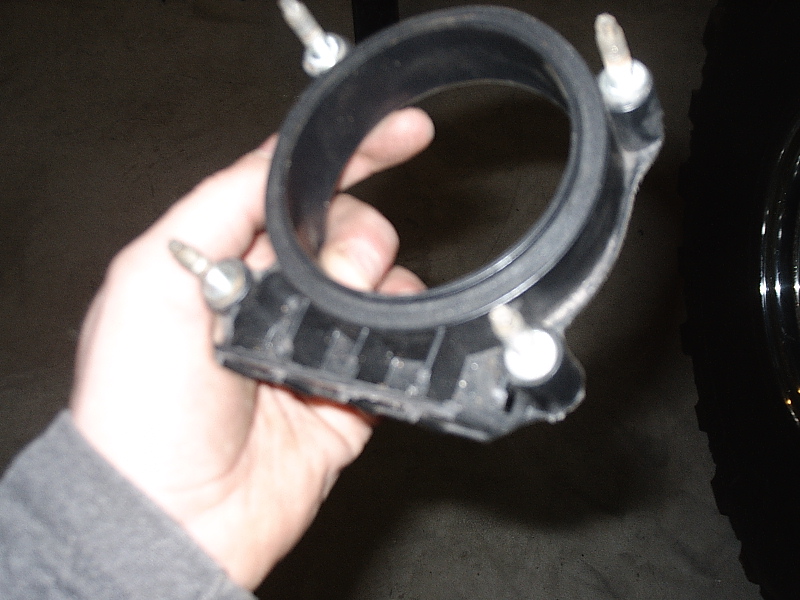 Hand holding a black flanged intake/throttle body adapter with mounting studs