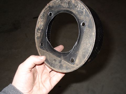 1996 Ford Bronco - A hand holds a dirty, circular metal part with four bolt holes, possibly a gasket or mounting plate.