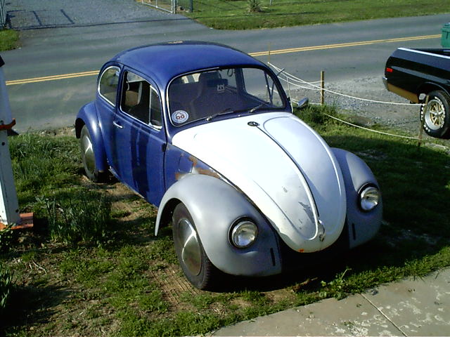 Blue and gray classic VW Beetle with white hood, mid-restoration, parked on grass near a road