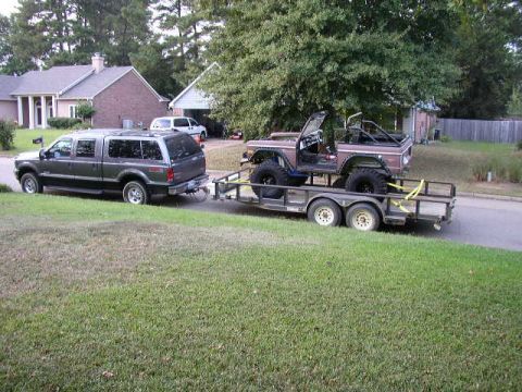1995 Ford Bronco - A brown Ford Bronco is loaded onto a trailer, which is being towed by a dark gray SUV.