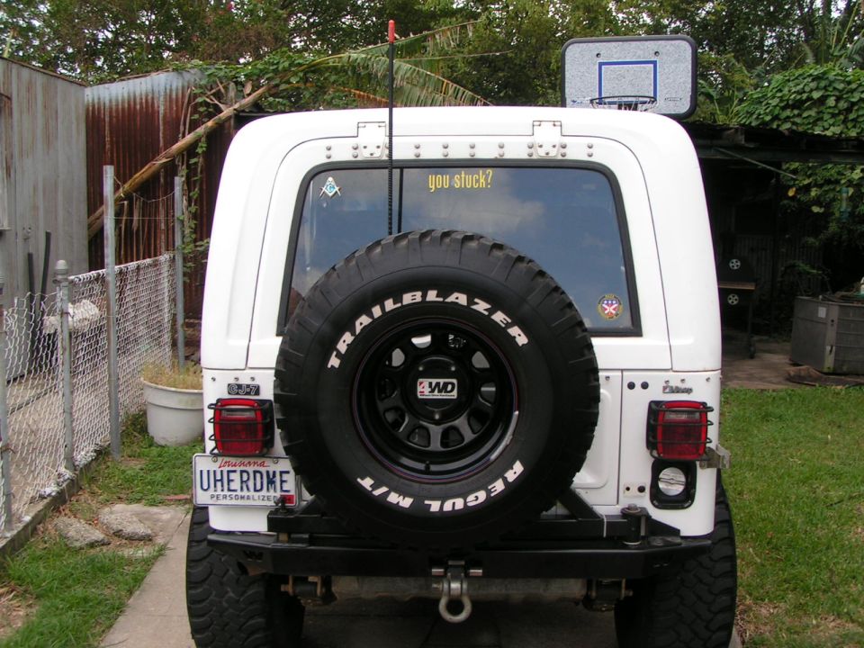 Rear of white Jeep CJ7 with spare tire, Louisiana UHERDME plate, and basketball hoop mounted on top.