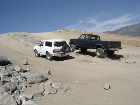 1988 Ford Bronco - Two Ford vehicles, a Bronco and an F-Series truck, navigate a rocky off-road course under a clear blue sky.