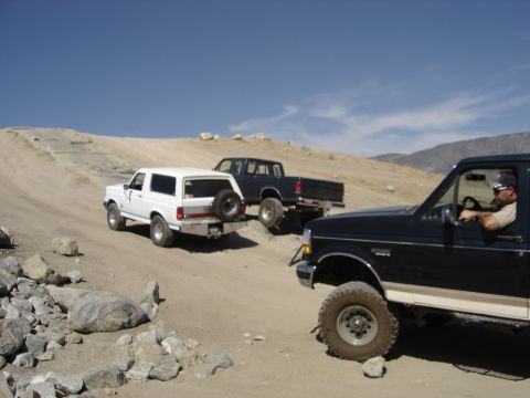 1988 Ford Bronco - Three trucks and SUVs navigate a dirt trail under a clear blue sky.