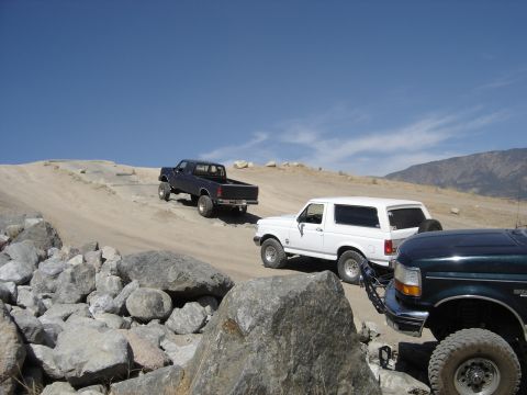 1988 Ford Bronco - Multiple off-road vehicles navigate a rocky, dusty trail under a clear blue sky.