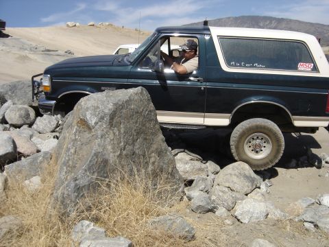1988 Ford Bronco - This Ford Bronco navigates a rocky trail, with a white camper shell and a visible MSD sticker on the rear window.