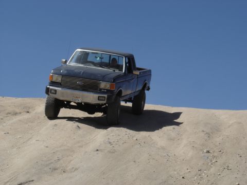 1988 Ford Bronco - This pickup truck, likely a 1987 model, navigates a sandy terrain under a clear blue sky.