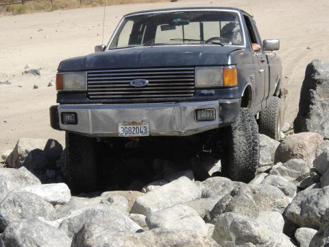 1988 Ford Bronco - Ford F-Series truck with aftermarket bumper driving over rocks.