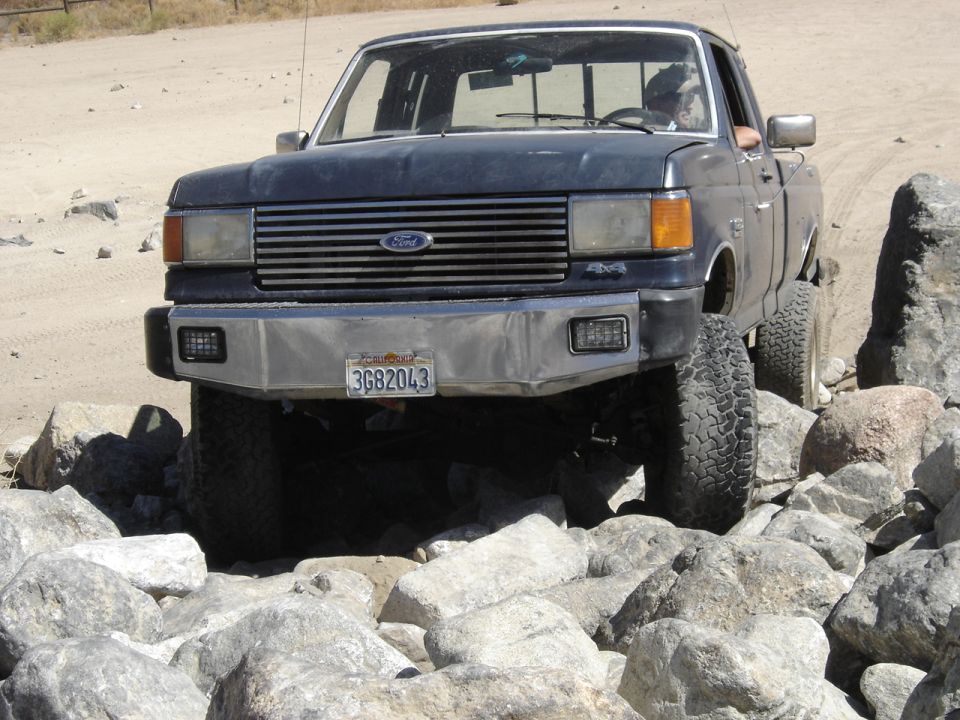 Dark blue Ford F-Series truck with aftermarket bumper navigating rocks. License plate 3G82043