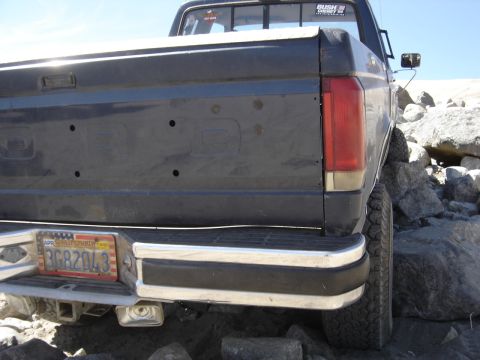 1988 Ford Bronco - A dark blue pickup truck is parked on rocky terrain, showing its rear end and license plate.