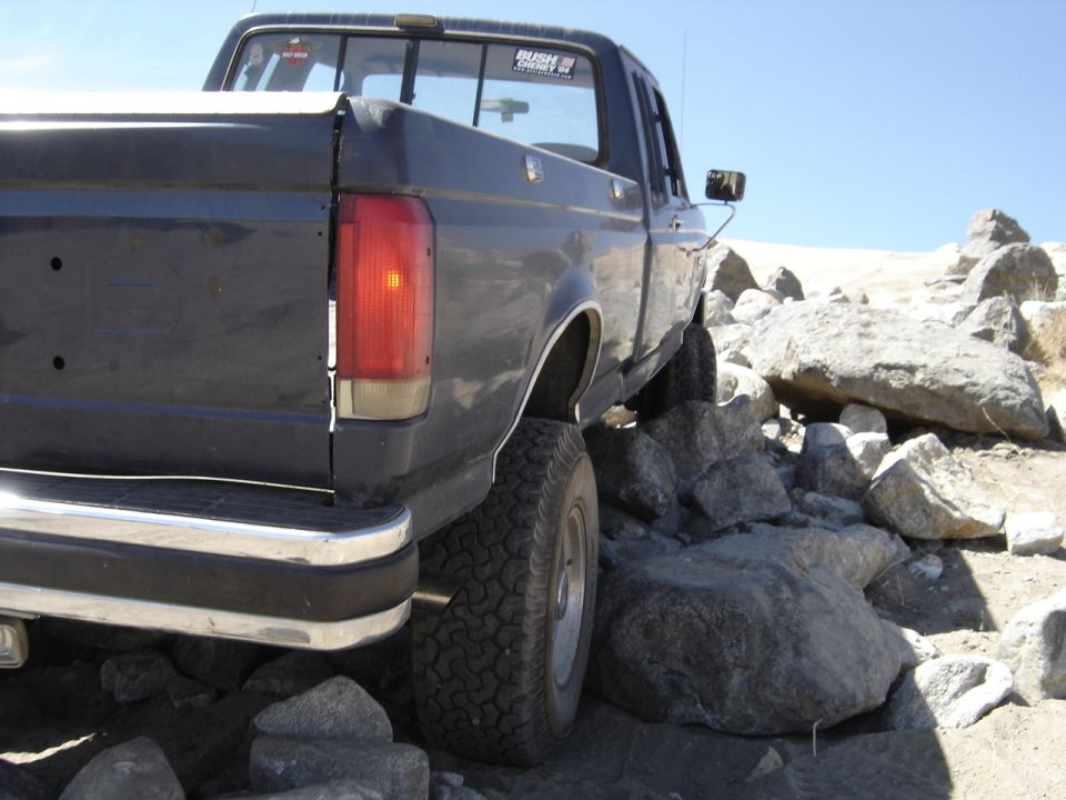 Rear view of dark blue pickup truck with off-road tires, navigating rocks