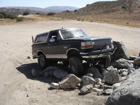 1988 Ford Bronco - This Ford Bronco is navigating a rocky trail in a dry, hilly landscape.