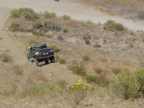 1988 Ford Bronco - A black Ford Bronco with a white top navigates a dusty trail in a dry, hilly landscape.