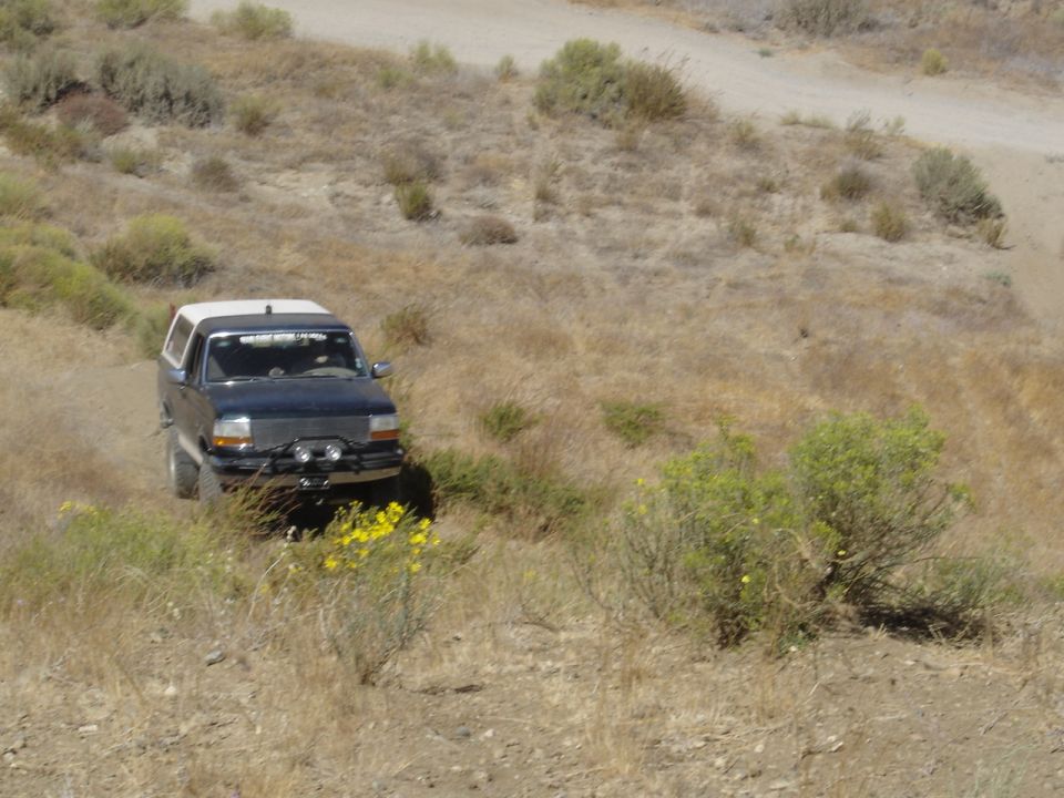 Dark blue 1992-1996 Ford Bronco with white camper shell driving on a dry, grassy hillside
