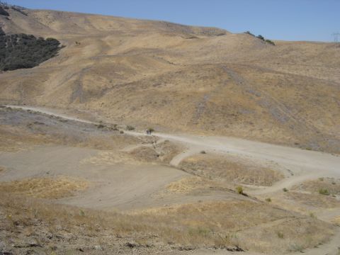 1988 Ford Bronco - A lone motorcycle navigates a dusty track in a vast, arid landscape.