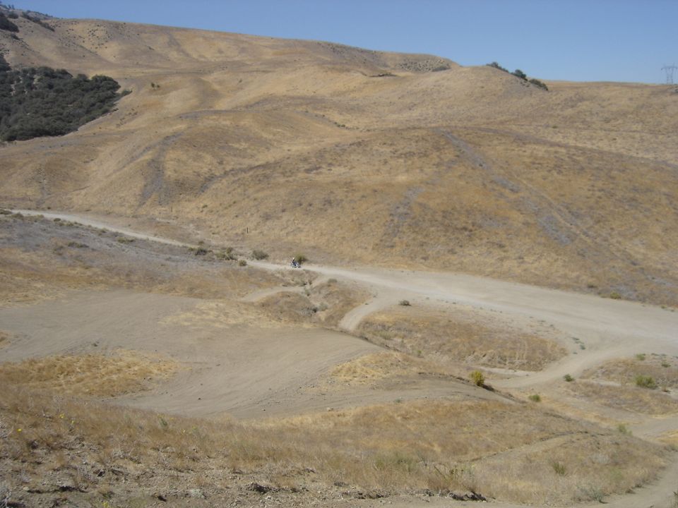 motorcycle riding on a dirt road through dry, rolling hills under a clear blue sky