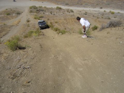 1988 Ford Bronco - A man watches a black Ford Bronco navigate a steep dirt incline in a dry, scrubby landscape.
