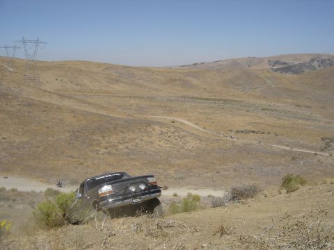 1988 Ford Bronco - A black Ford F-Series truck navigates a dusty, off-road trail with hills and power lines in the background.