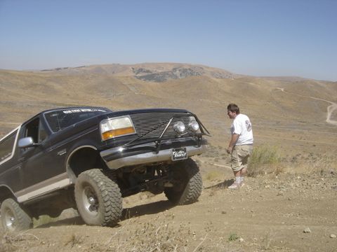 1988 Ford Bronco - A man watches a lifted Ford Bronco navigate a dusty, arid landscape with hills in the background.