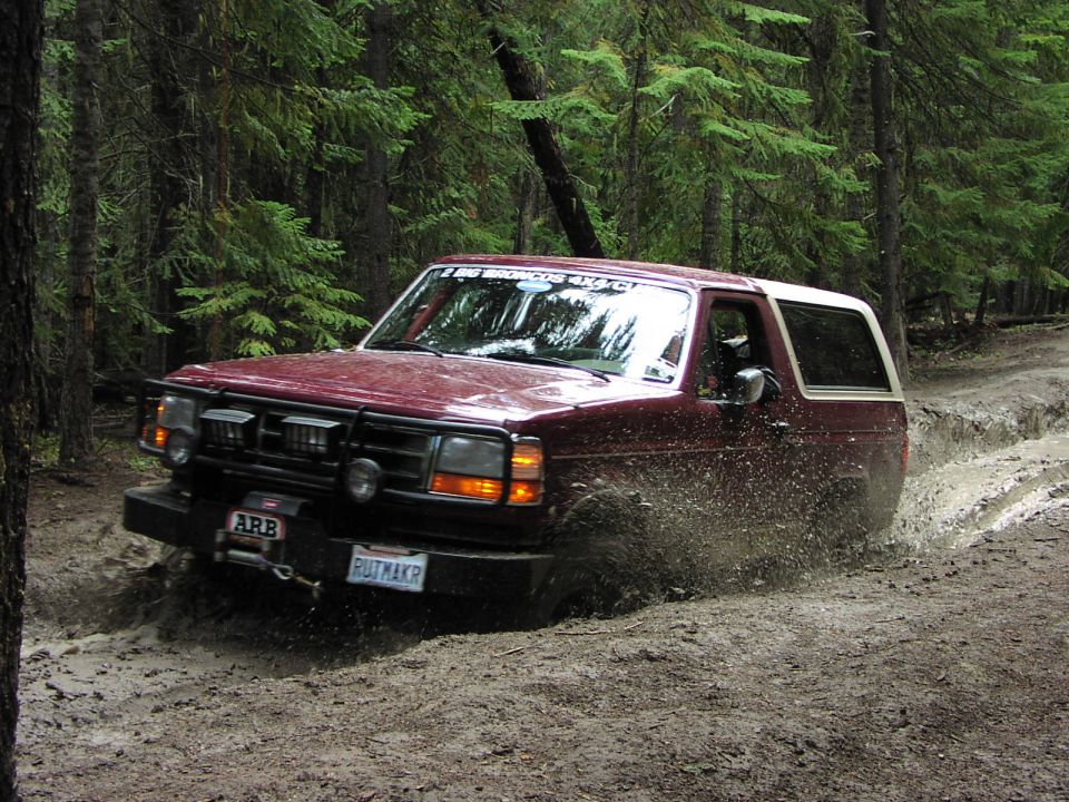 Maroon Ford Bronco with ARB bumper and winch splashing through a muddy forest trail