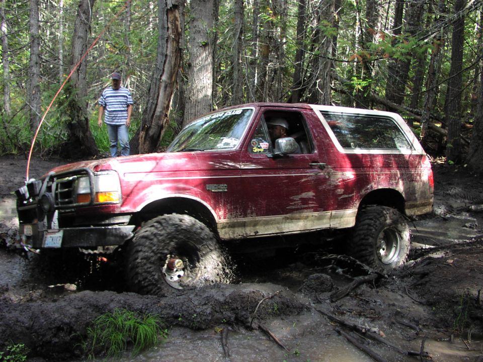 Red lifted Ford Bronco on mud tires sitting in a deep muddy trail rut in the woods