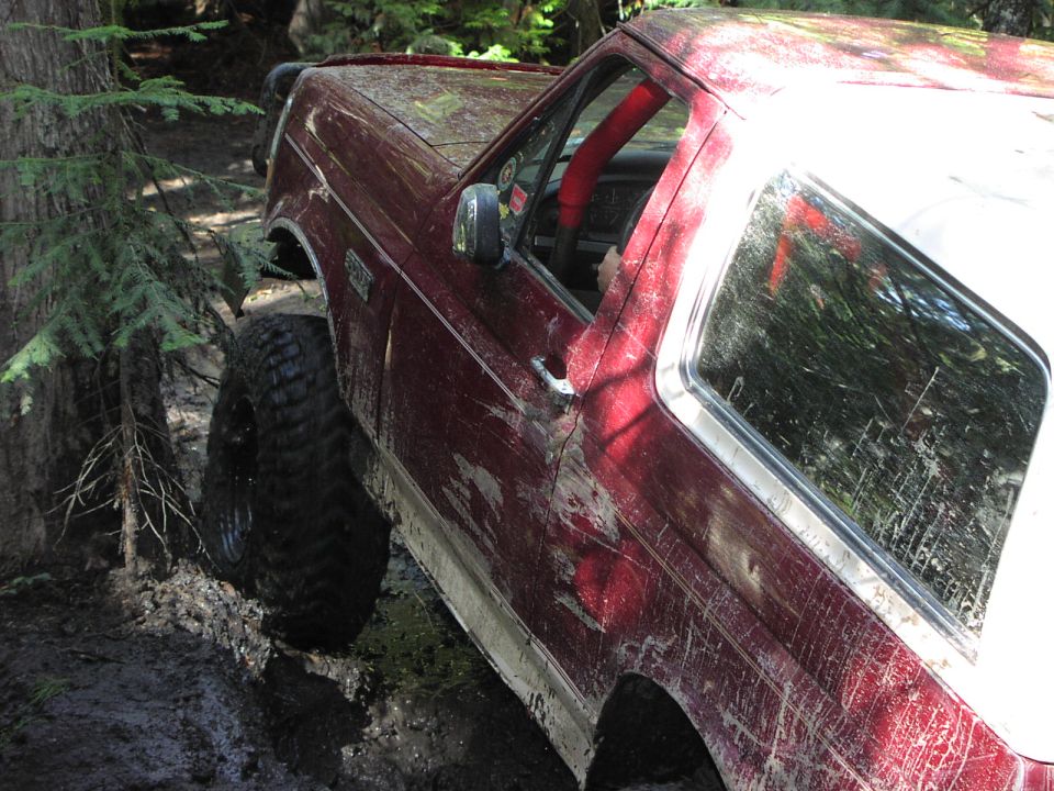 Close-up of mud-splattered red Bronco body side with white top and large off-road tire