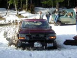 1993 Ford Bronco - Two Ford Broncos are seen in a snowy outdoor scene, with the front vehicle partially stuck in the snow.