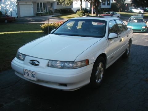 1993 Ford Taurus - A white sedan is parked in a driveway with other vehicles in the background.
