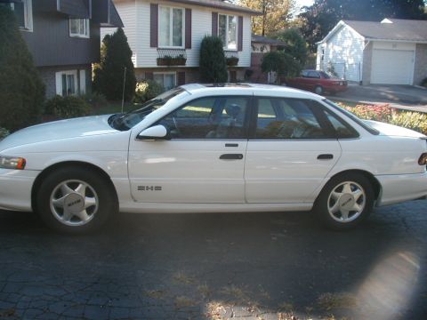 1993 Ford Taurus - A white 1993 Ford Taurus sedan is parked in a driveway on a sunny day.