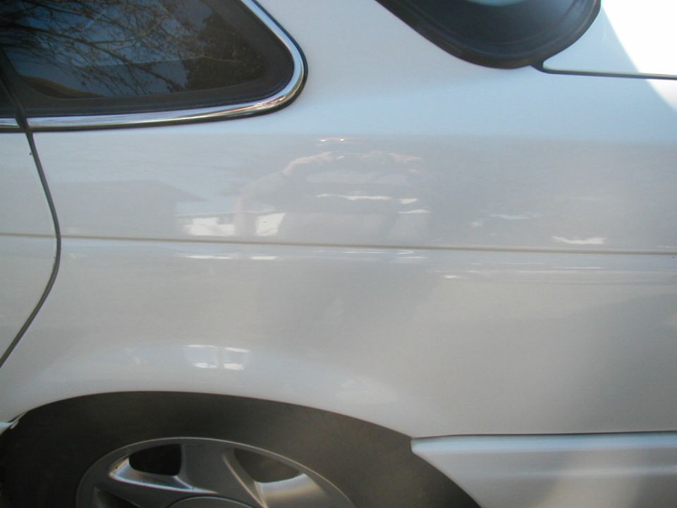 Close-up of a white sedan rear quarter panel with chrome window trim and alloy wheel
