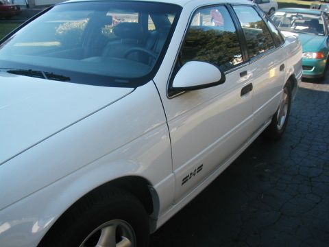 1993 Ford Taurus - A white 1993 Ford Taurus sedan is parked outside, with another green vehicle visible in the background.