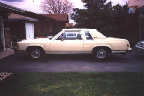 1985 Ford LTD Crown Victoria - Side profile of a cream two-door Ford LTD Crown Victoria coupe with a padded half vinyl roof, wire-look wheel covers and thin bodyside mold…