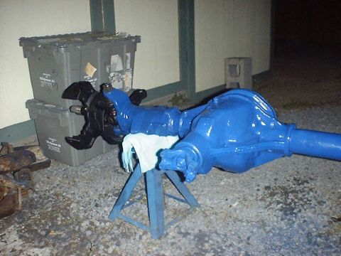 1988 Ford Bronco - A front axle assembly, painted bright blue, rests on a stand next to trash bins.