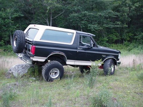 1993 Ford Bronco - Ford Bronco is shown off-road, with its rear tire resting on a large rock.