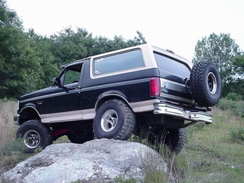 1993 Ford Bronco - This Ford Bronco is positioned on a large rock, showing its off-road capabilities and rear-mounted spare tire.