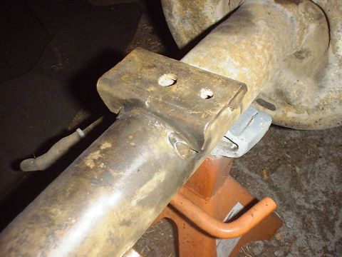 1988 Ford Bronco - Close-up of a vehicle's rear axle assembly, supported by an orange jack stand, with visible rust and a metal bracket.