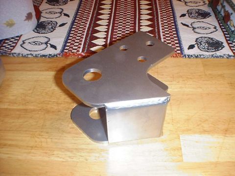 1988 Ford Bronco - A bare-steel double-shear frame bracket standing on a butcher-block table, made from two laser/plasma-cut side plates welded to a folded sp…