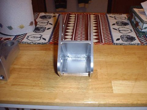 1988 Ford Bronco - End-on view down the open channel of a bare-steel double-shear bracket standing on a butcher-block table, showing the internal weld beads j…