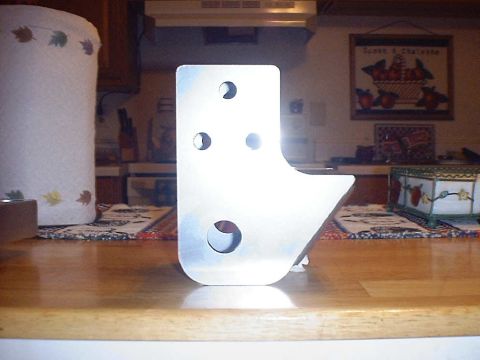 1988 Ford Bronco - A bare aluminum shock or link mounting bracket stands on end atop a wooden kitchen counter, with four drilled holes of varying size, rounde…